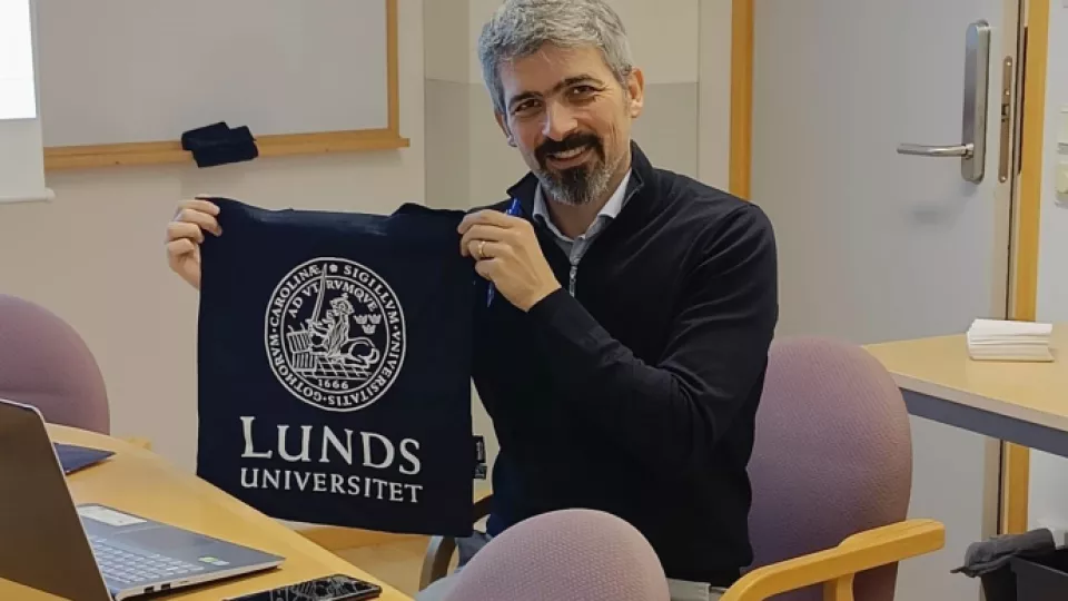 Photograph of Vincenzo Covello holding up a fabric bag with the Lund University logo. 