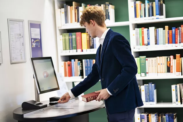 A student is using the self service machine to borrow a book. Photo.