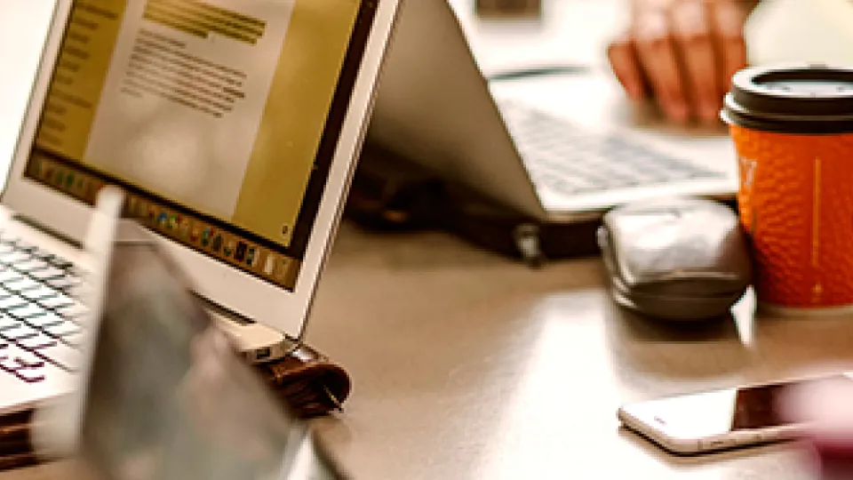 Photograph showing the hands and laptop of two people working at a table,