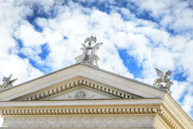 Photo of a part of a roof of an antique building with the blue cloudy sky as a background.