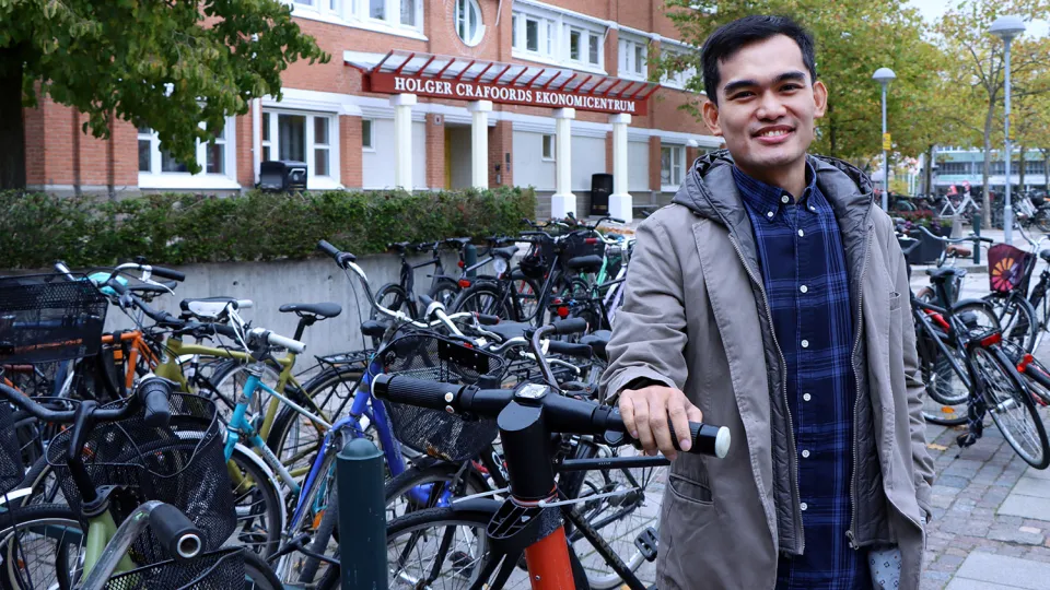 A person standing outside, with bikes and e-scooters around him. Photo.