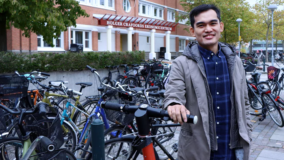 A person standing outside, with bikes and e-scooters around him. Photo.