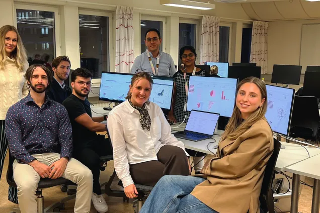 Six students sitting in front of screens showing dashboards, in a computer laboration room. 