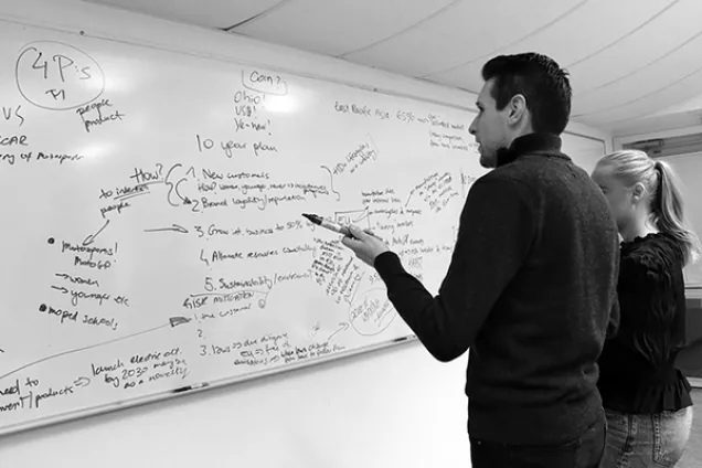Two persons in front of a filled whitebord. Photo