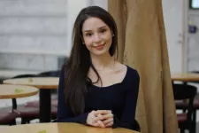 Photograph of Megan Andrews sitting by a round table and smiling at the camera. 