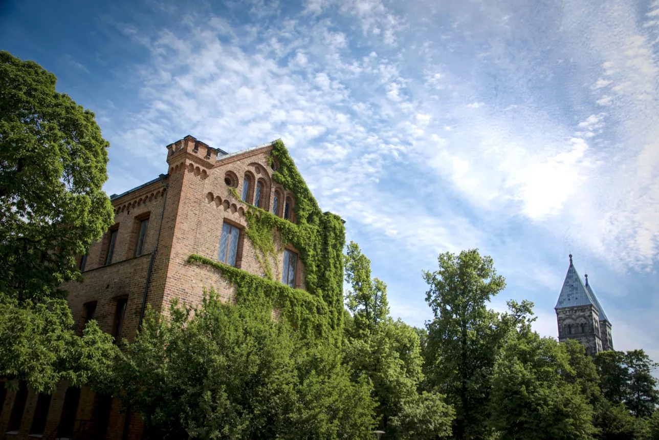 Bild tagen underifrån av en äldre byggnad omgiven av grönska och blå himmel